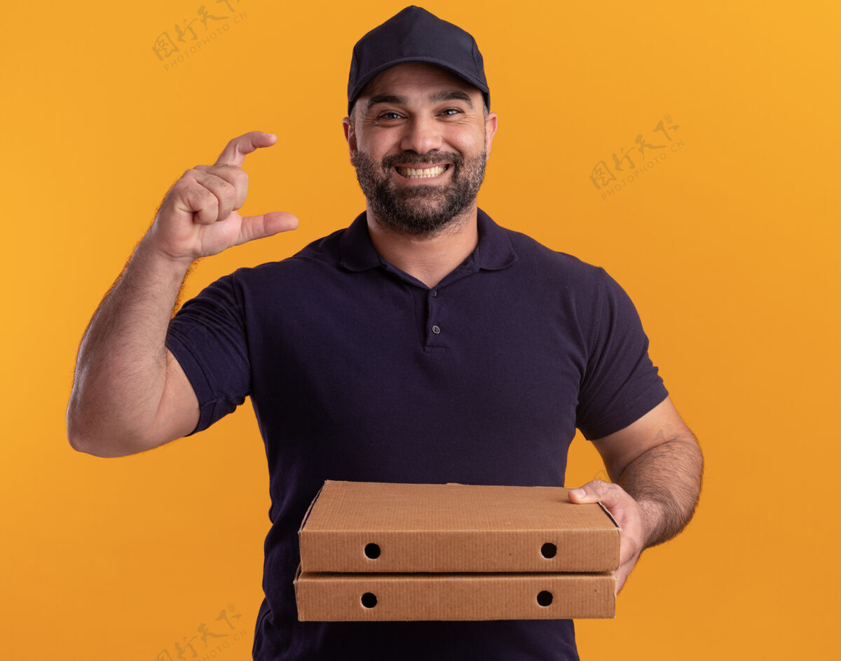 大小微笑着的中年送货员 穿着制服 戴着帽子 拿着披萨盒 黄色的墙上孤立地显示着大小披萨制服中年