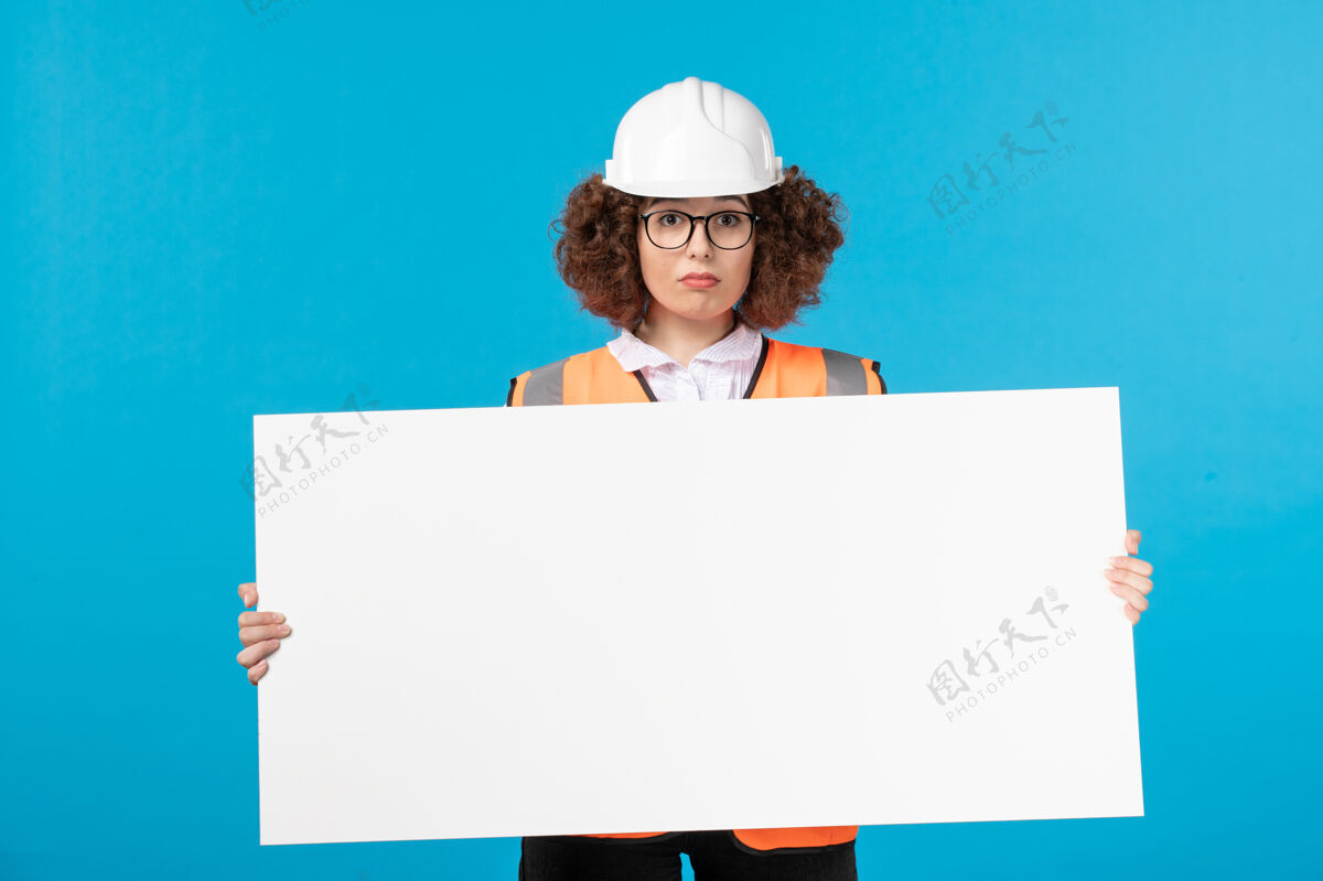 女性身着制服的女建筑工人正拿着蓝色墙壁上的普通办公桌工作建筑商背心