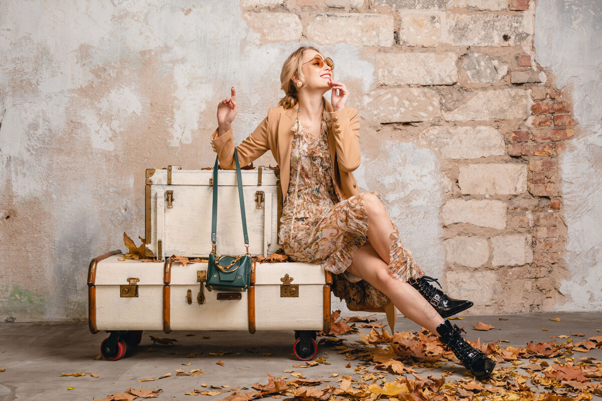 外套在街上 穿着米色外套的金发美女坐在手提箱上对着墙季节包美丽