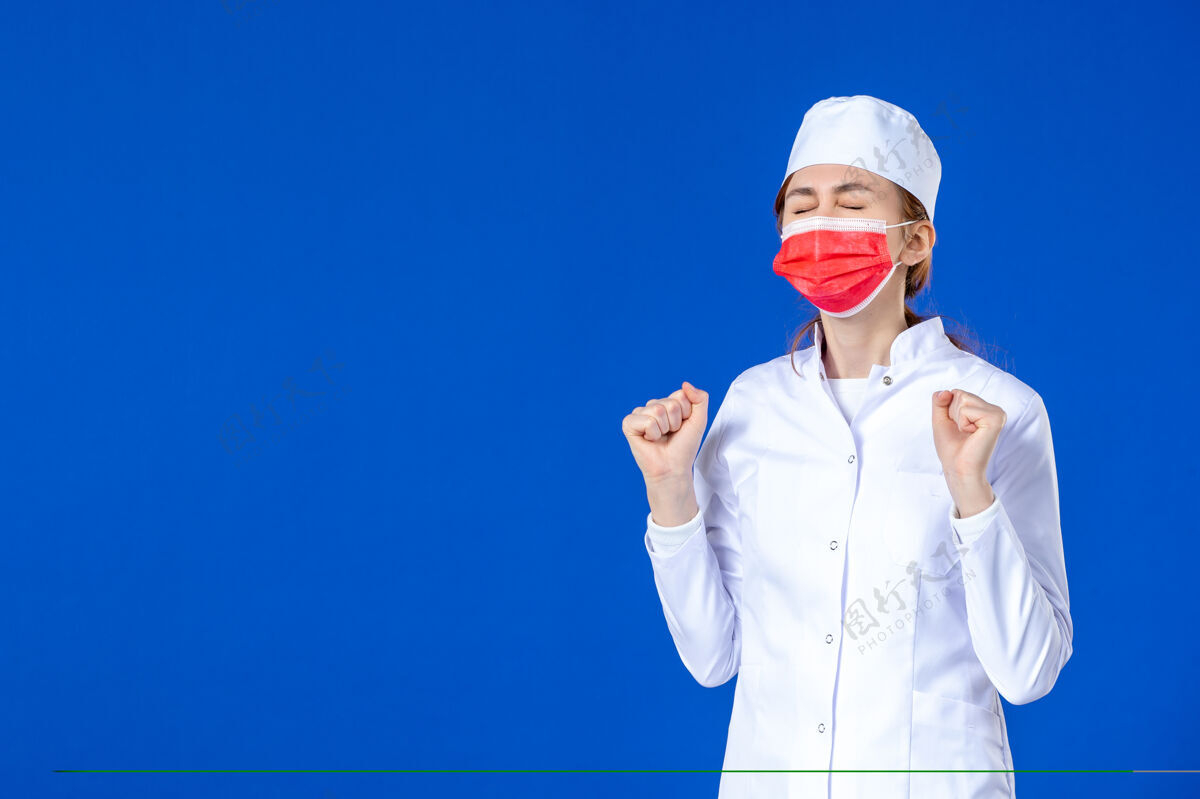 专业正面图身着医疗服的年轻护士 蓝色墙上戴着红色防护面具防护蓝色年轻护士
