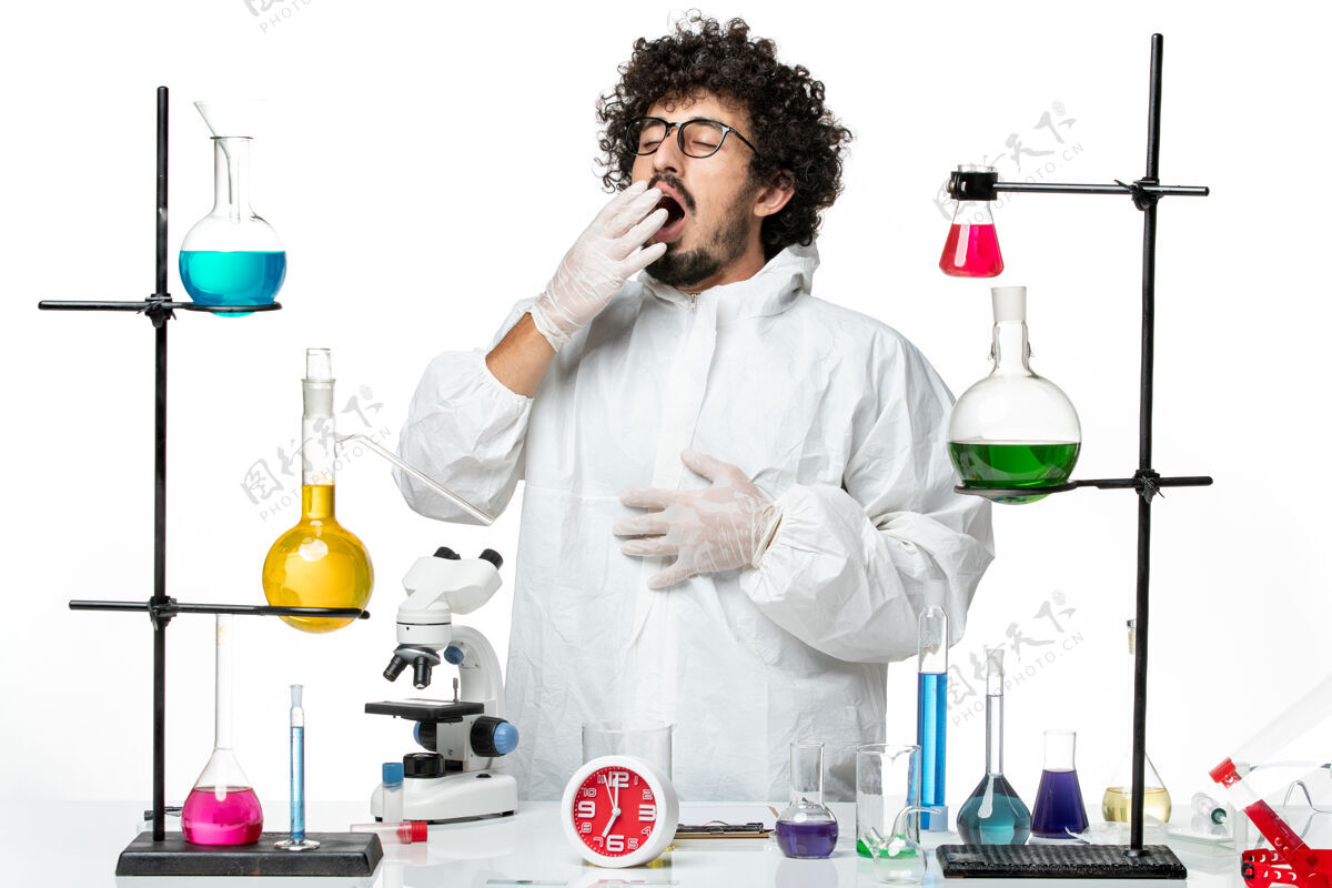 站着正面图身着白色特殊套装的年轻男性科学家站在桌子旁打呵欠科学化学打哈欠