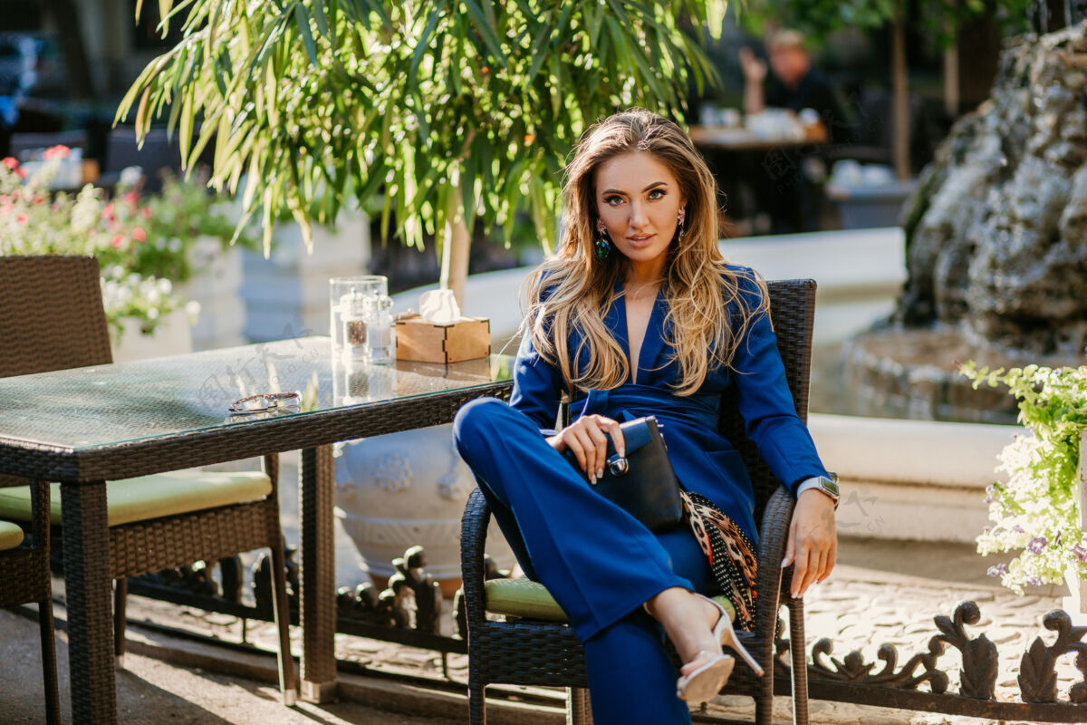 春天在阳光明媚的秋日里 一位身着优雅蓝色套装的微笑美女坐在咖啡馆里夹克女性性感