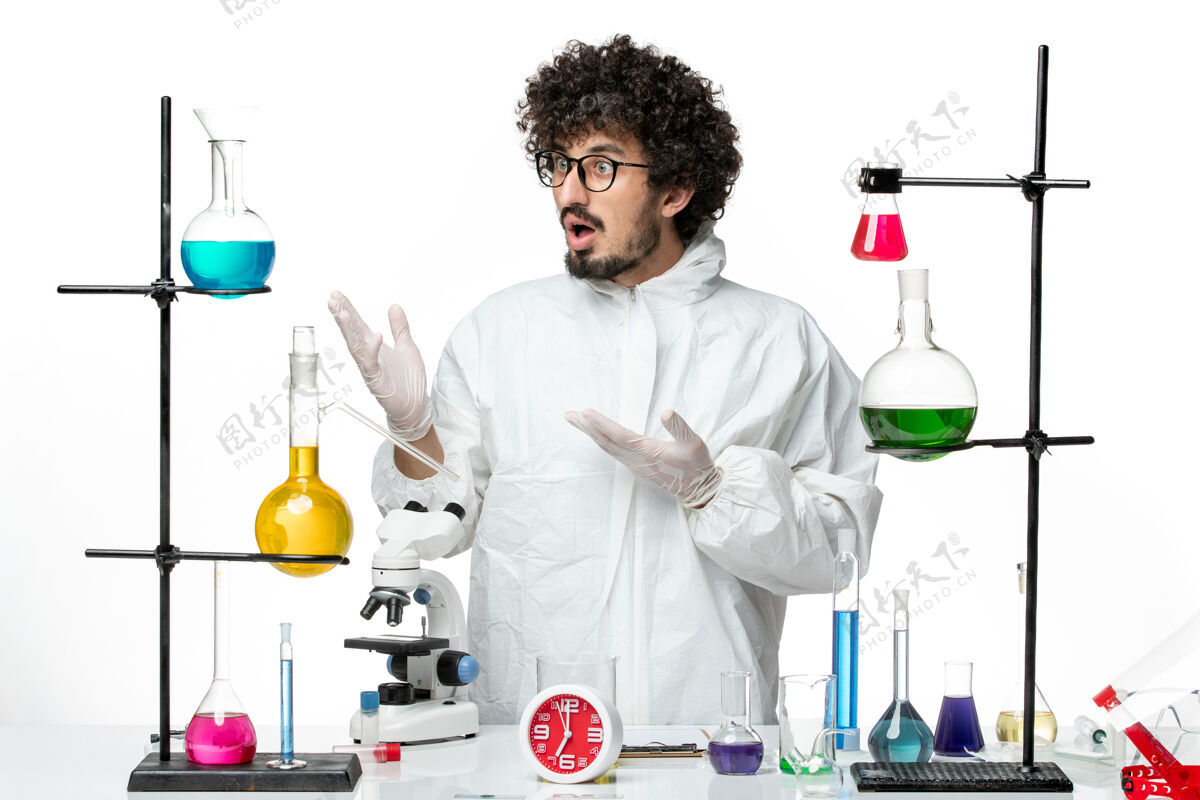 实验室正面图：身着特殊套装的年轻男性科学家站在桌子旁 在白色的实验室办公桌上拿着解决方案立场周围理科