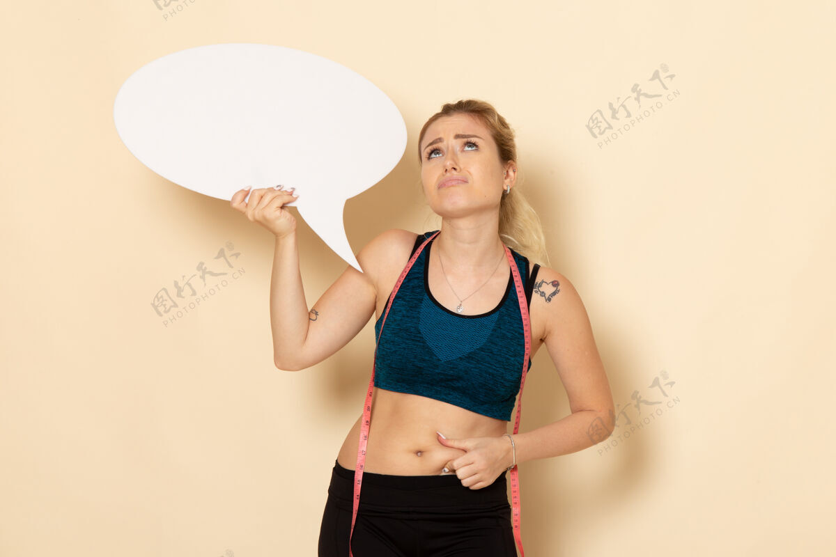 办公桌正面图身穿运动装的年轻女性手持白色标牌 在白色办公桌上测量自己的身体身体健康运动美容健身操美丽运动健身