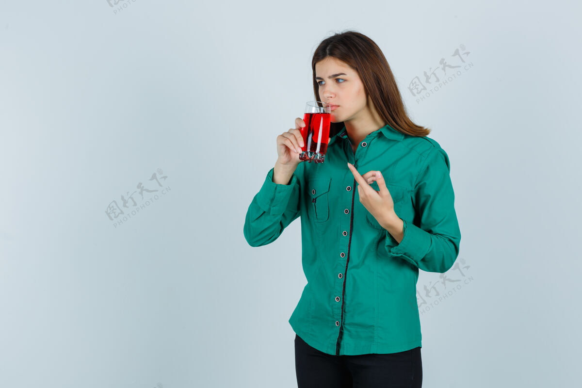 办公室年轻女孩喝着一杯红色的液体 穿着绿色上衣 黑色裤子 用食指指着它 目光集中前视图学校作业非洲种族教育