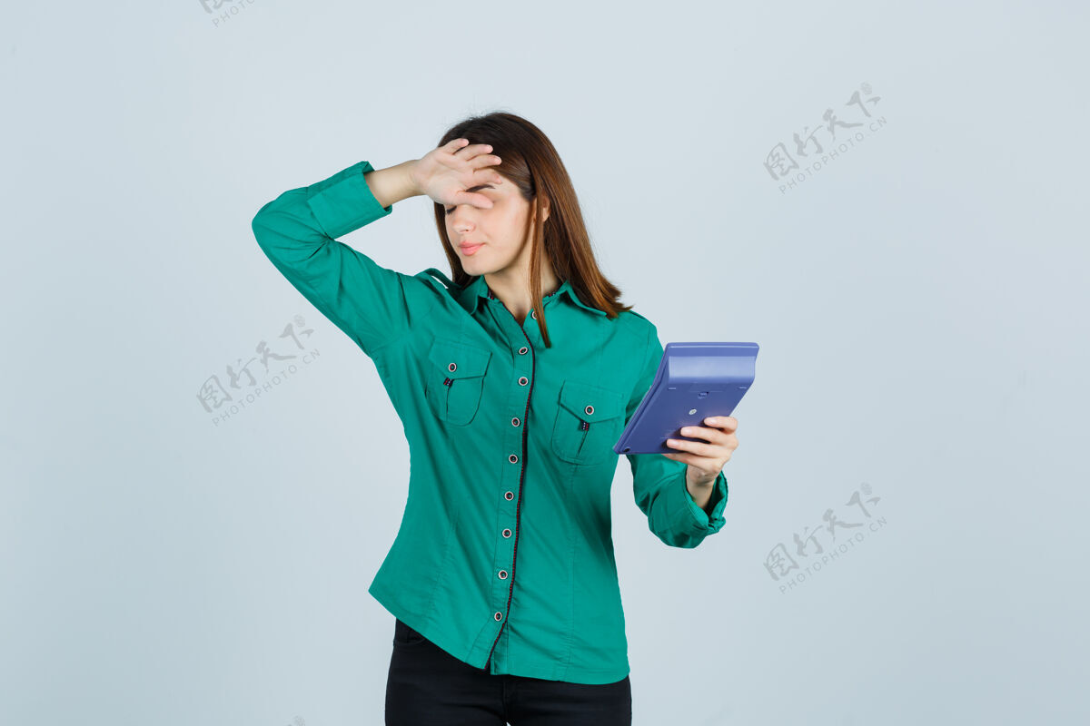 成人年轻女士拿着计算器 手放在额头上 穿着绿色衬衫 看上去很沮丧前视图女尖叫保持