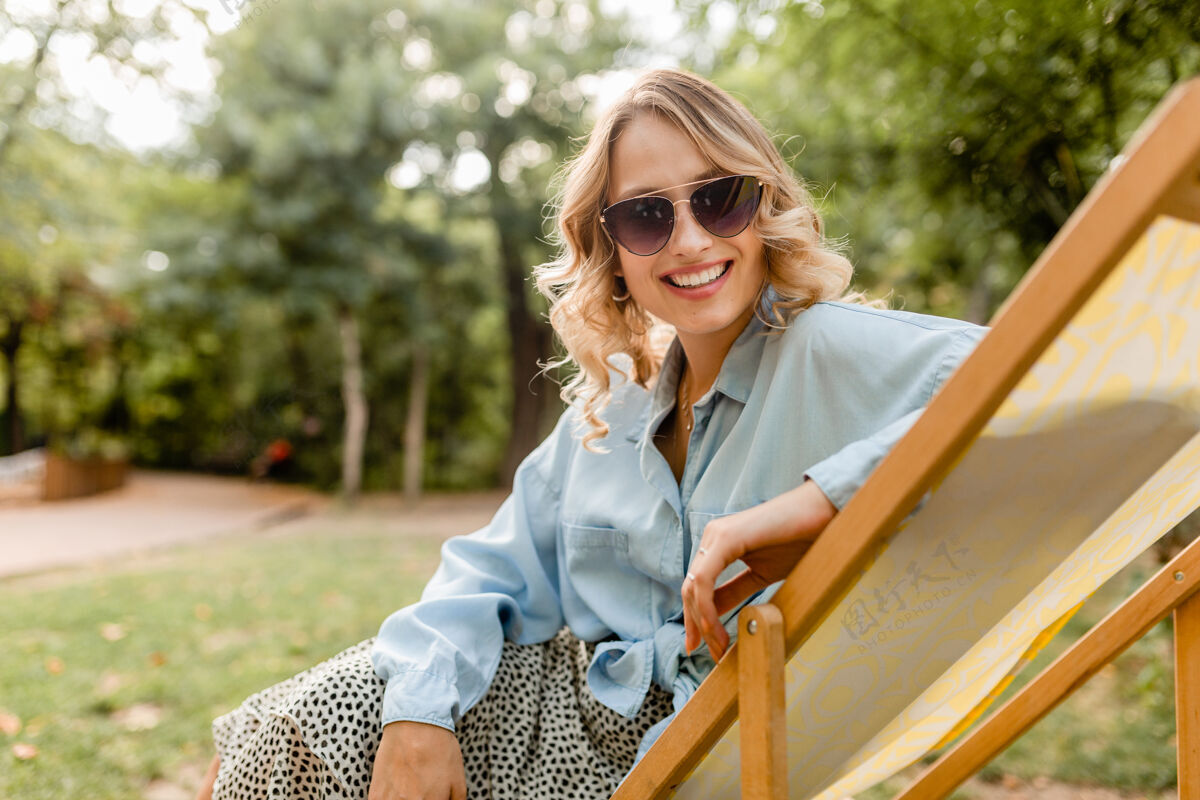 衣服迷人的金发微笑的女人坐在躺椅上穿着夏天的衣服快乐休闲穿