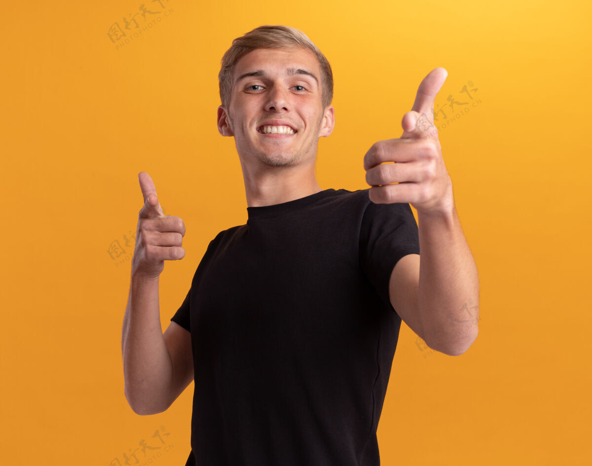男人微笑着的年轻帅哥 穿着黑色衬衫 在黄色的墙上向你展示孤立的姿态穿微笑衬衫