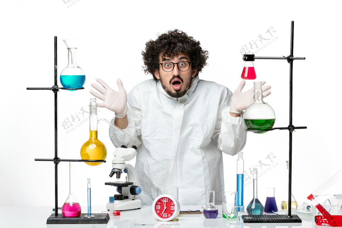 实验室正面图身着特殊套装的年轻男性科学家站在桌子旁 在白色的墙上拿着解决方案实验室视图周围