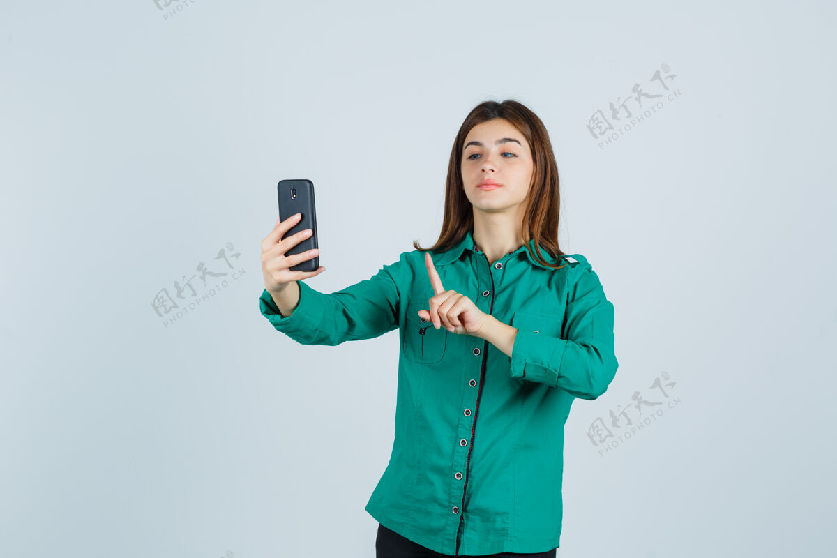 视频穿着绿色上衣 黑色裤子的年轻女孩在打视频电话时 表现出一种保持一分钟的姿势 看起来很可爱 正面视图裤子房子显示