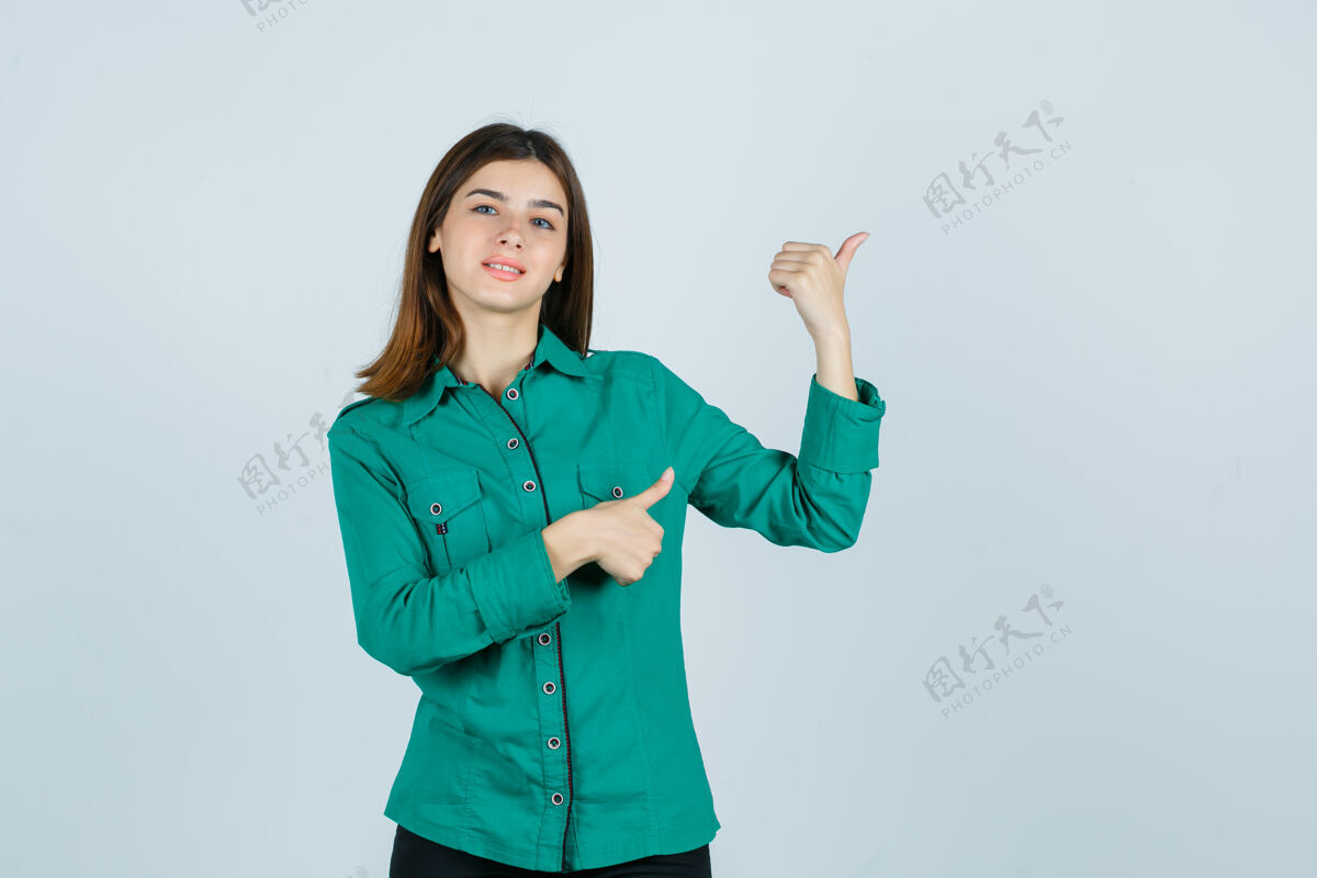微笑年轻的女性指着右上角 拇指穿着绿色衬衫 看起来很高兴前视图成人年轻娱乐