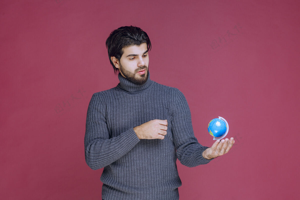 年轻男人拿着一个蓝色的迷你地球仪 聚精会神地看着它促销姿势学生