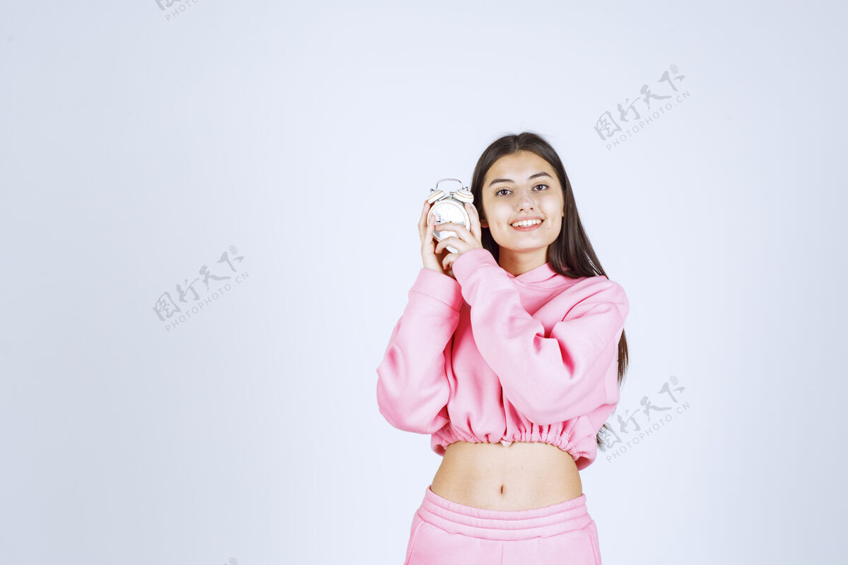 女性一个穿着粉色睡衣的女孩拿着一个闹钟 把它当作一个产品来推销方便聪明摄影
