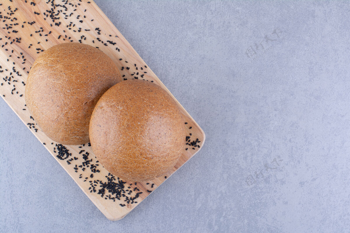 烘焙食品小木板上放着黑芝麻和汉堡包 放在大理石表面种子早餐面粉