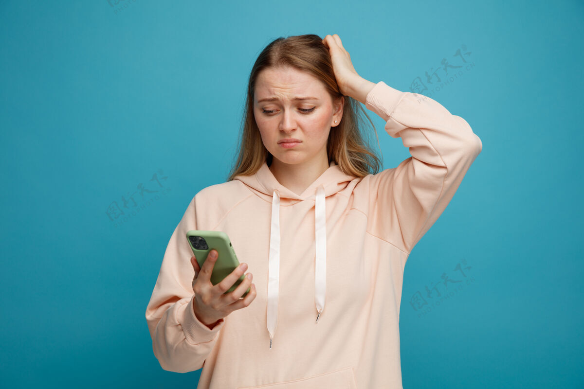 手机遗憾的是 年轻的金发女郎手抱头看手机后悔蓝色女人