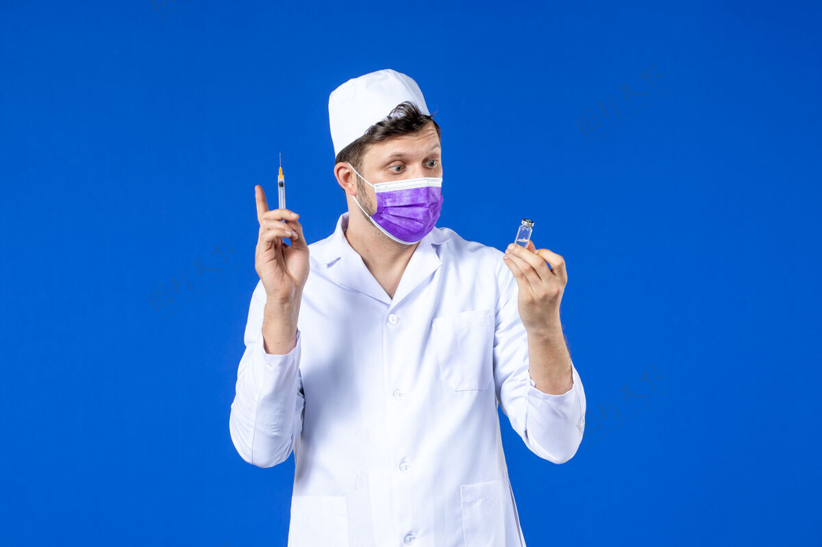 实验室外套前视图中的男医生穿着医疗服和口罩持有疫苗和注射在蓝色男医生大流行药品