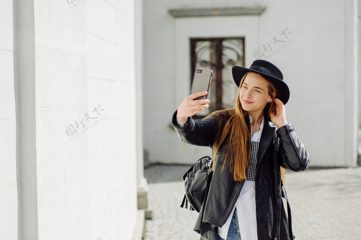 通信户外夏日写真的年轻时尚女孩在阳光明媚的日子摆在街上与手机移动触摸短信