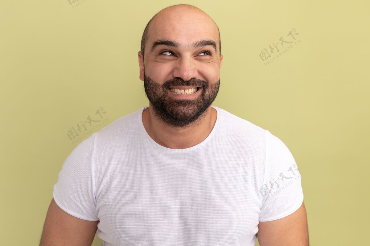 胡子快乐的胡子男人穿着白色t恤 脸上带着微笑 站在绿色的墙上靠边站起来伙计