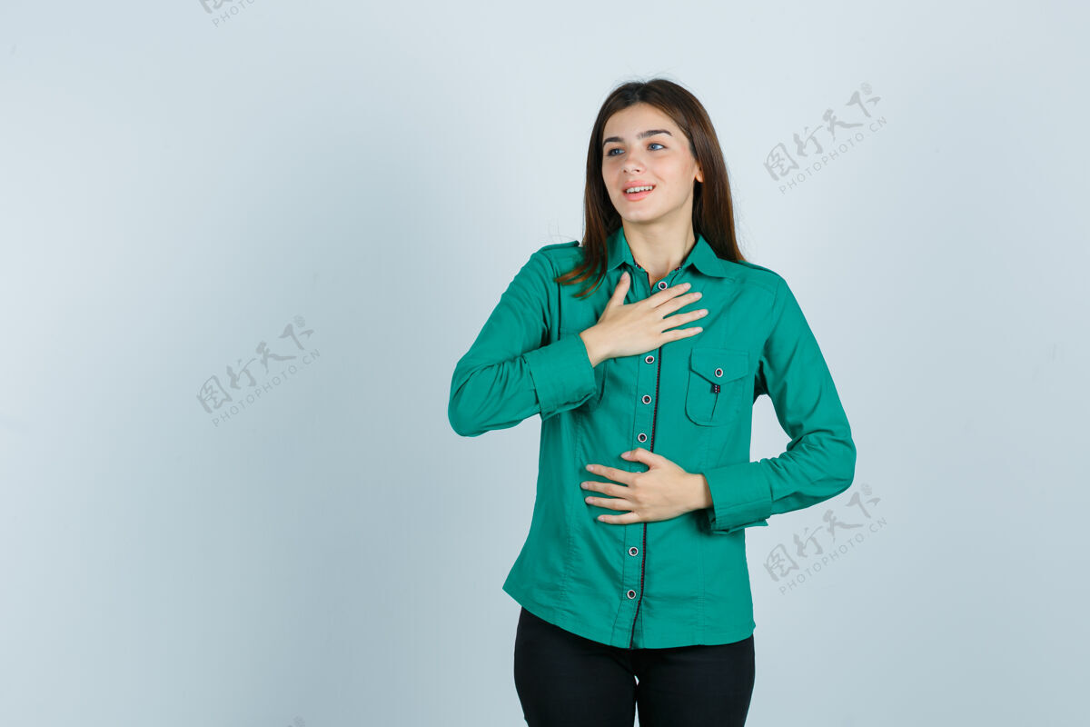 女孩年轻女孩一只手放在胸前 另一只手放在肚子上 穿着绿色上衣 黑色裤子 看起来很开心正面图模特女性欢呼