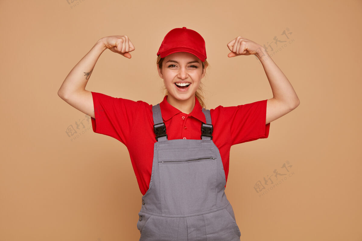制服兴奋的年轻女建筑工人穿着制服 戴着帽子做着坚强的手势姿势帽子工人