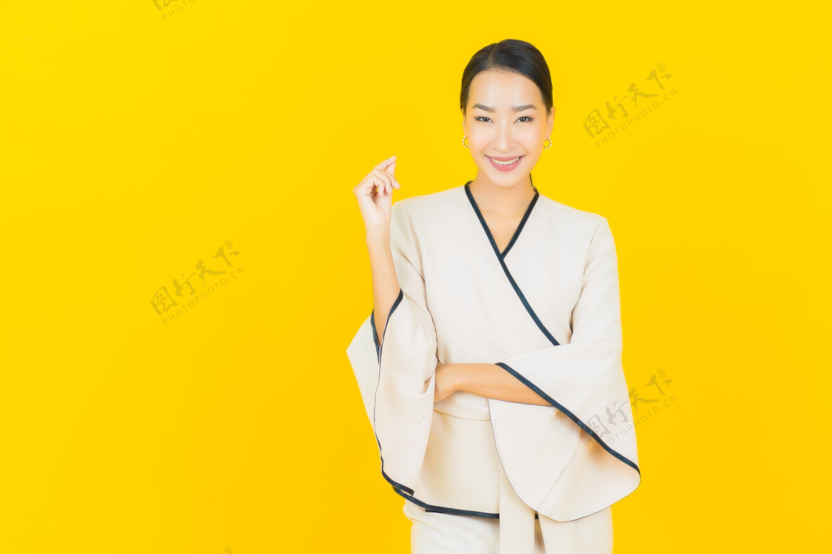 时尚美丽的亚洲年轻商业女性在黄色墙上穿着白色西装微笑的画像朋友成人工人