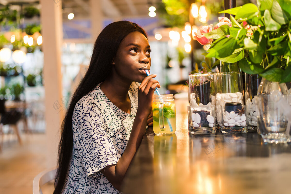 配料快乐的非洲裔美国妇女在咖啡厅喝一杯天然柠檬水排毒饮料女士非洲咖啡馆