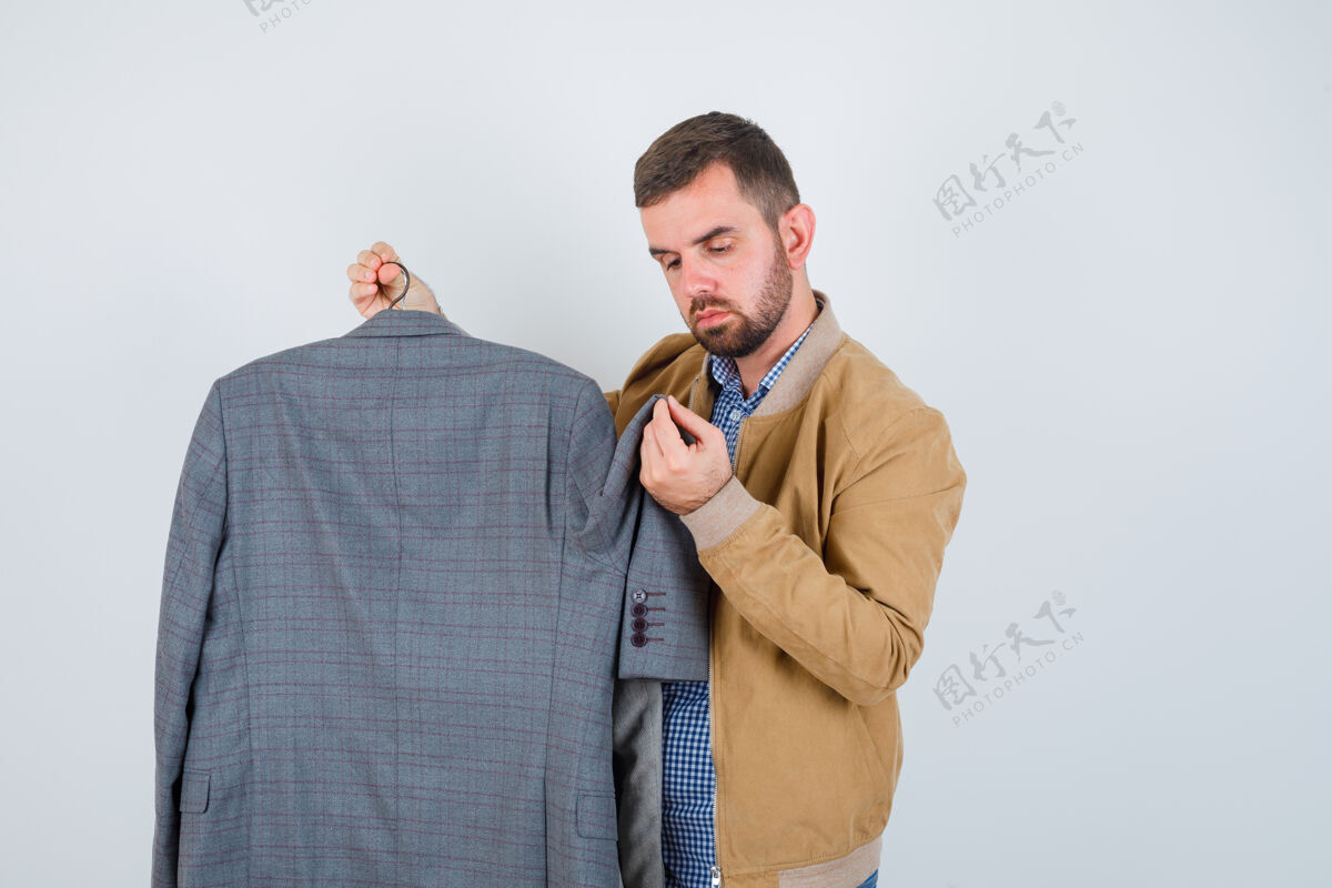 男人穿着夹克衫的年轻人看着西装 侧着身子站着 神情茫然选择胡须思想