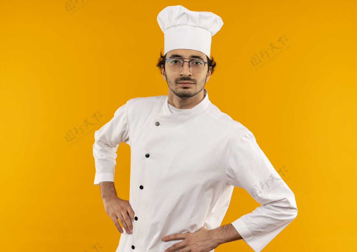 男人自信的年轻男厨师穿着厨师制服 戴着眼镜 双手放在臀部制服厨师穿着