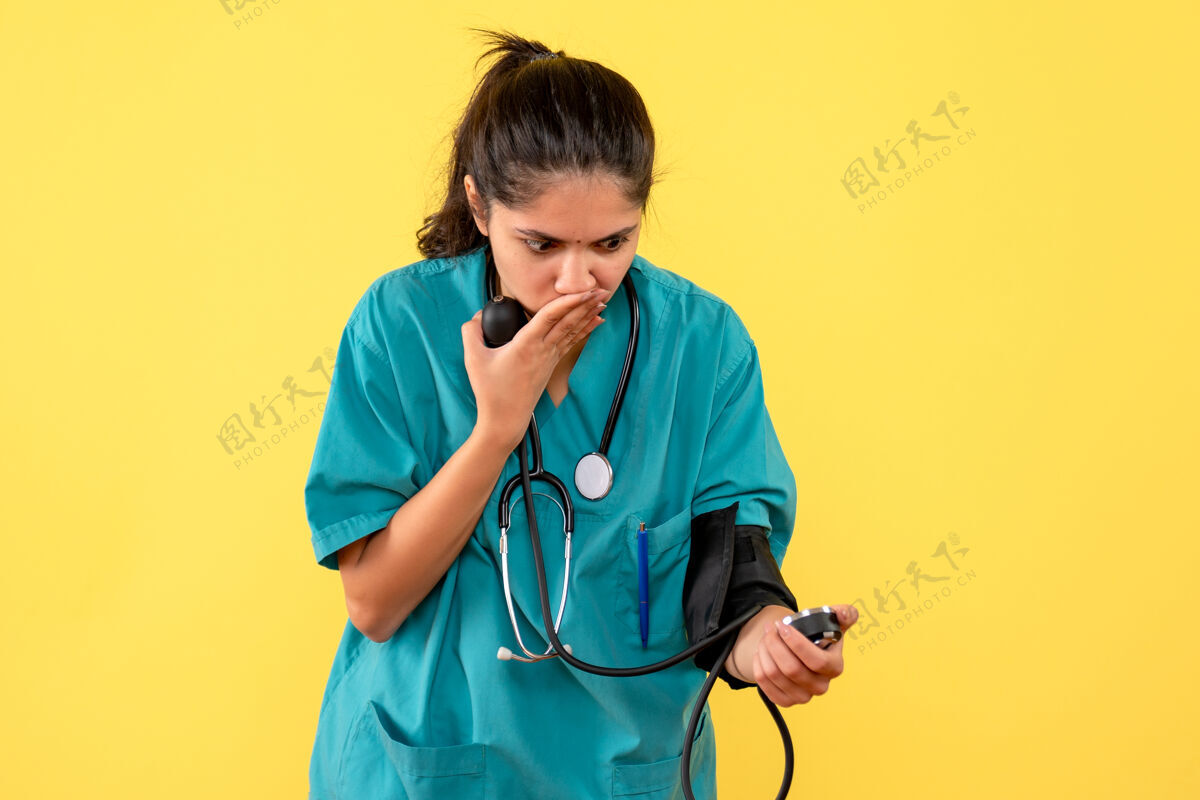 设备前视图震惊女医生穿着制服使用血压计站在黄色背景正面人物使用