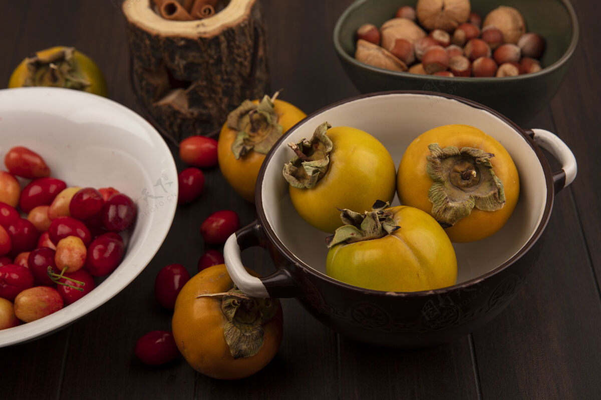 肉桂白色碗上美味的科尼莉亚樱桃俯视图 柿子水果放在碗上 坚果放在碗上 肉桂棒放在木制表面的木罐上水果美味坚果