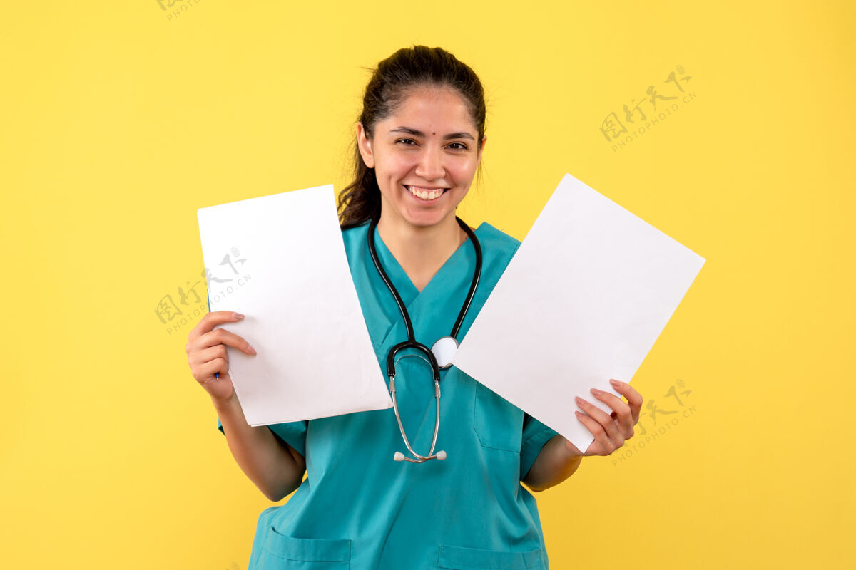手正面图黄色背景上 穿着制服的女医生双手拿着纸大笑人员人员听诊器