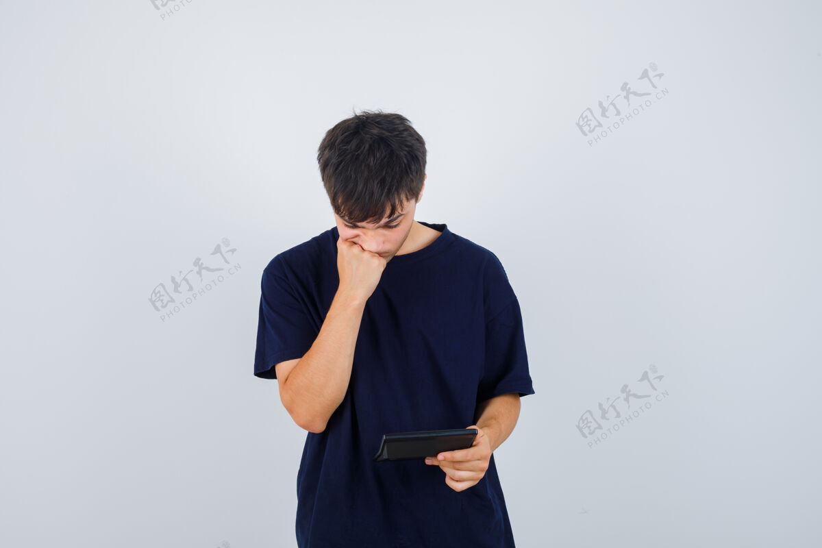 休闲年轻人看着计算器 穿着黑色t恤 用拳头托着下巴 看上去很困惑前视图肖像计算器下巴