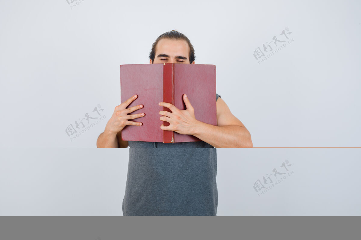 连帽衫年轻男子穿着无袖连帽衫 脸上抱着翻开的书 看起来很困倦 前视英俊工作工人