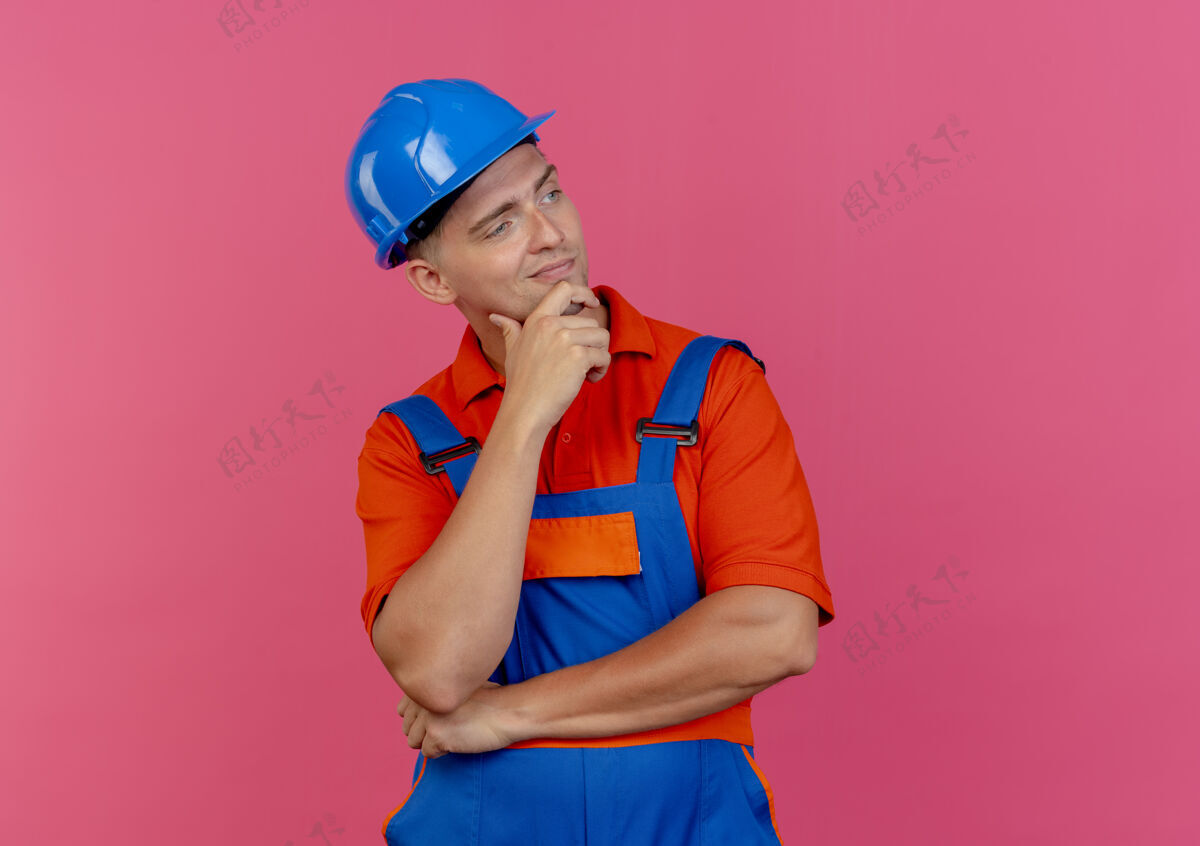 制服看着旁边高兴的年轻男建筑工人穿着制服 戴着安全帽 手放在下巴下面头盔粉色请戴
