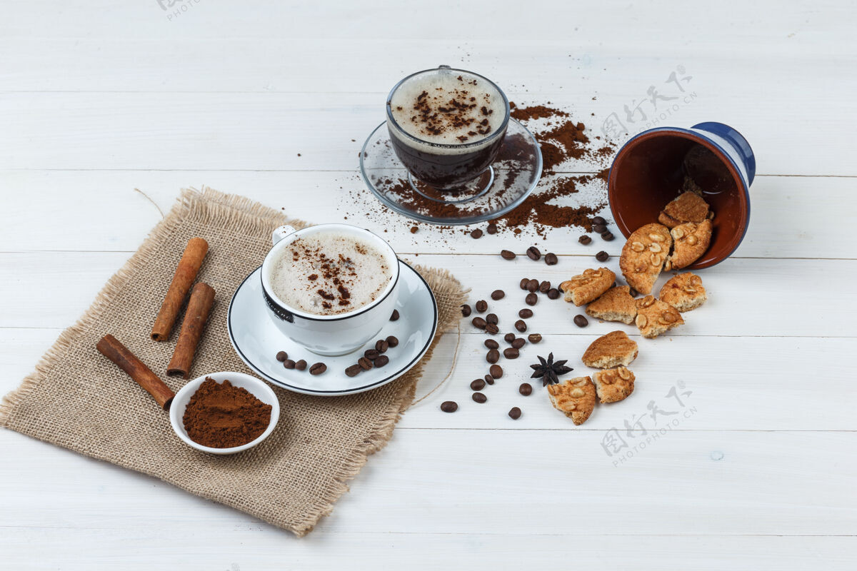 早晨一套咖啡豆 磨碎的咖啡 曲奇饼 肉桂棒和咖啡杯在木制和布袋背景高角度视图咖啡因肉桂卡布奇诺