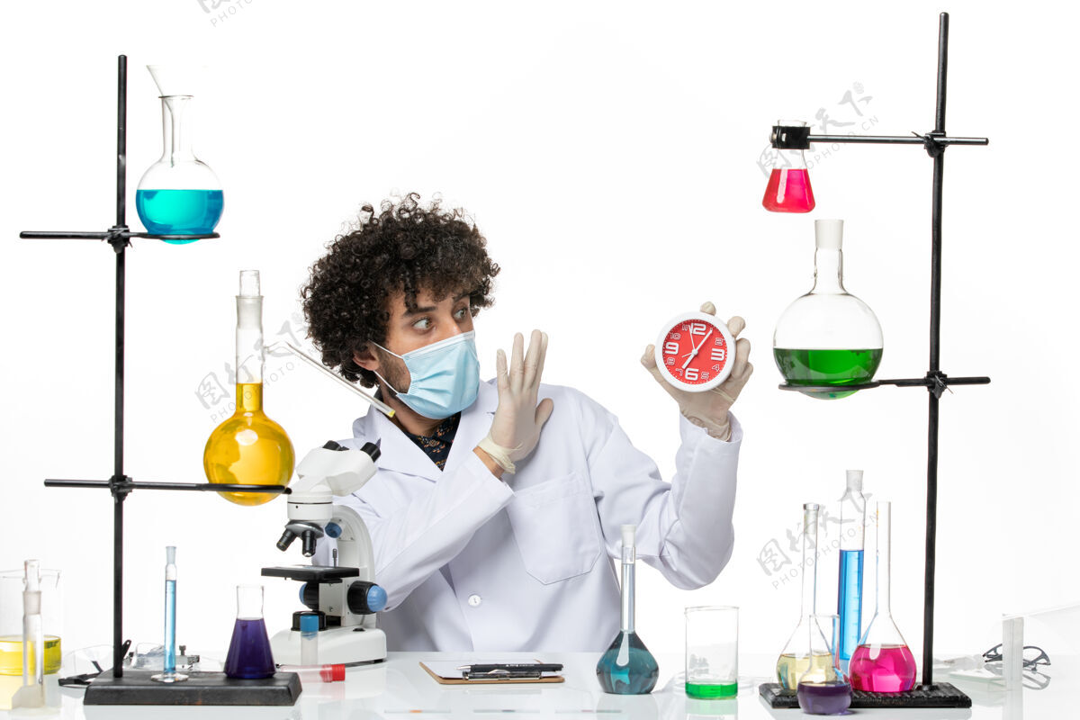 男性前视图男性化学家穿着医疗服 戴着面罩 在浅白色的空间里拿着时钟医学浅白实验室