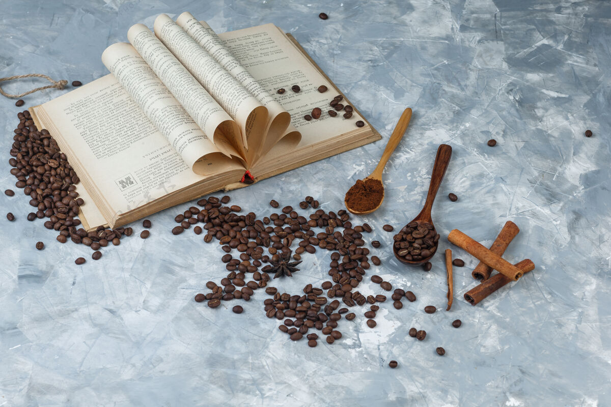 咕噜一套磨碎的咖啡 书 肉桂棒和咖啡豆放在一个木制勺子里 背景是灰色的 高角度的视角卡布奇诺质地咖啡