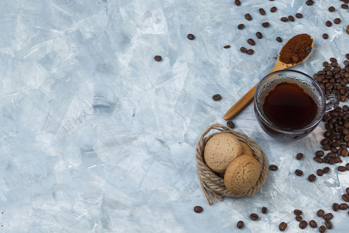 早晨一些咖啡豆 一杯咖啡和咖啡粉放在木勺里 饼干 浅蓝色大理石背景上的绳子 平放卡布奇诺讨论豆子