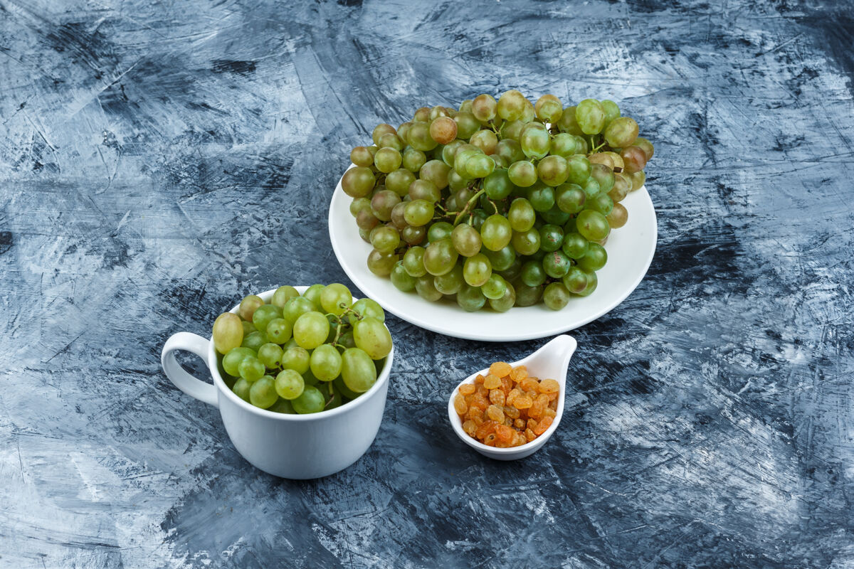 季节高角度观看绿色葡萄在白色盘子和杯子里 葡萄干在粗糙的石膏背景上水平酒庄食物健康