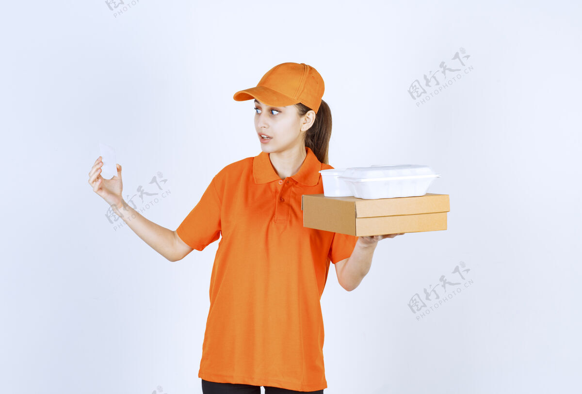 促销身着橙色制服的女快递员在出示名片时 手里拿着一个纸板箱和一个塑料外卖箱模特年轻人服务