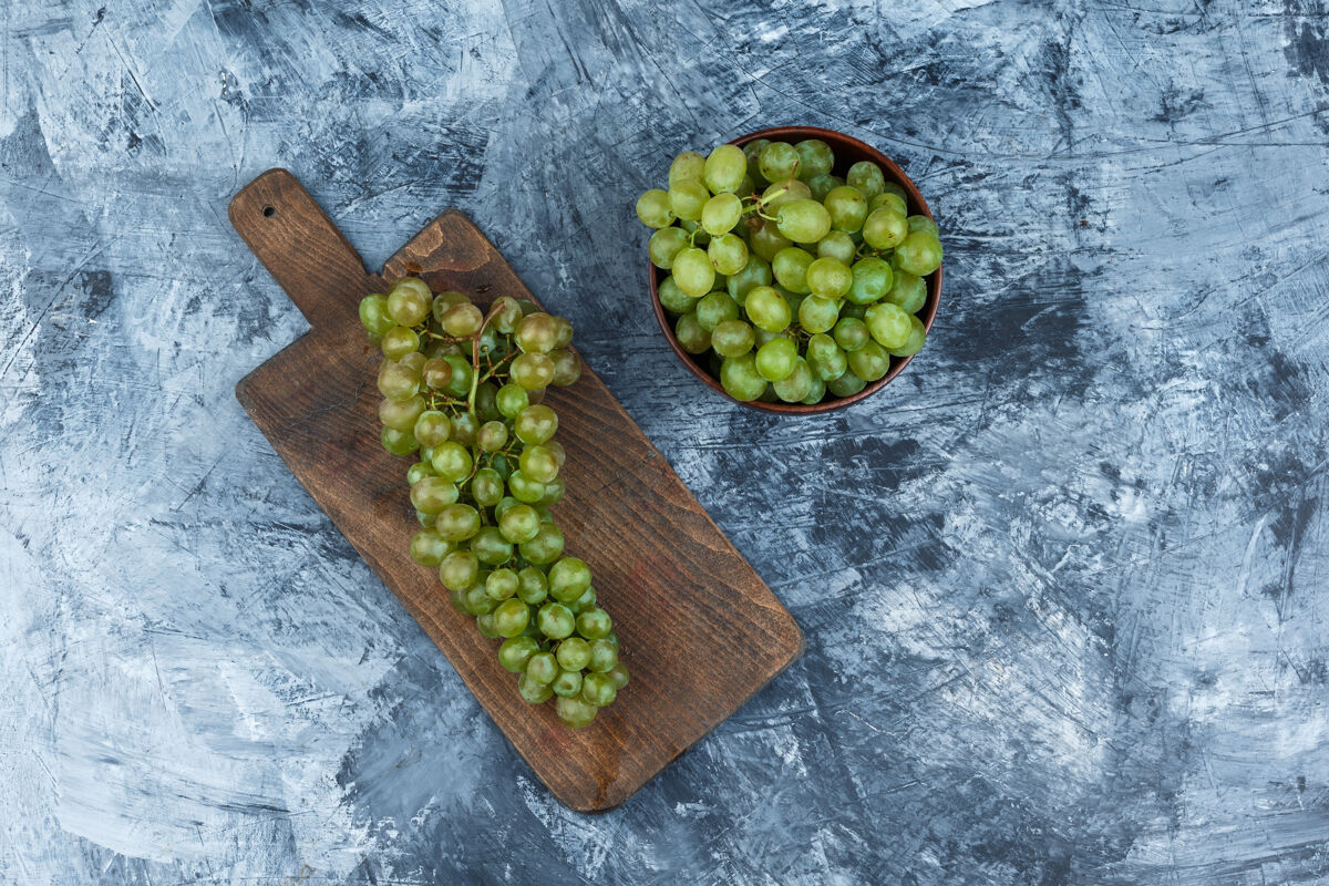 水果把白葡萄放在砧板上 把白葡萄放在深蓝色大理石背景上的碗里平铺葡萄藤酒庄木板