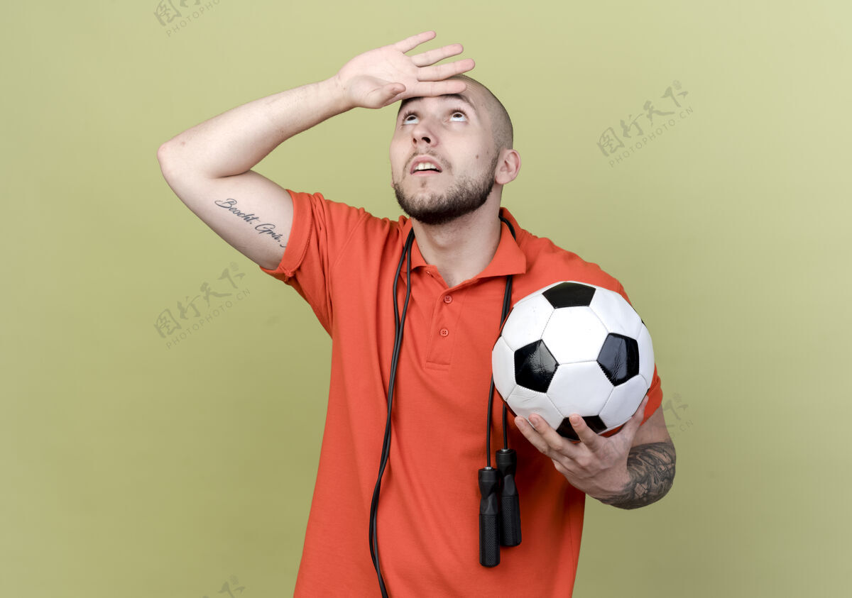 向上看着肩上扛着跳绳 拿着球 手放在额头上的年轻运动型男子橄榄绿色年轻
