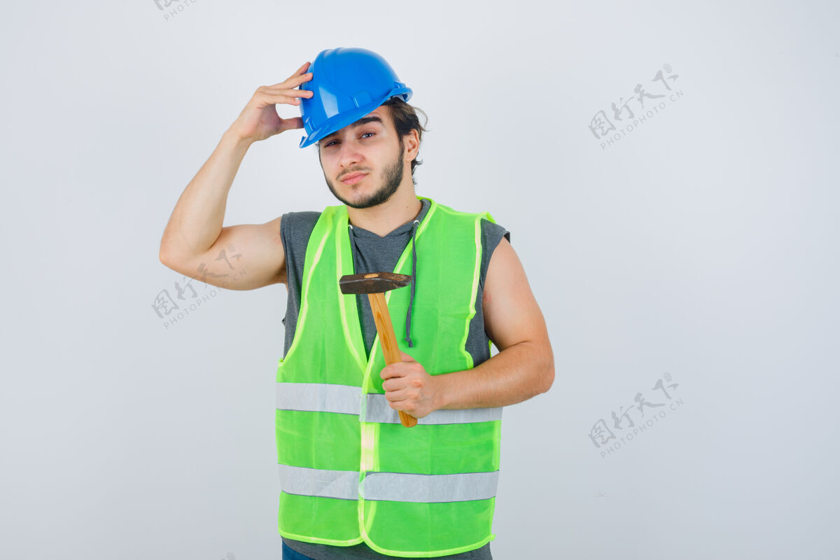 成人年轻的建筑工人手持锤子 手放在头上 穿着工作服 看上去很自信锤子工作服欢呼