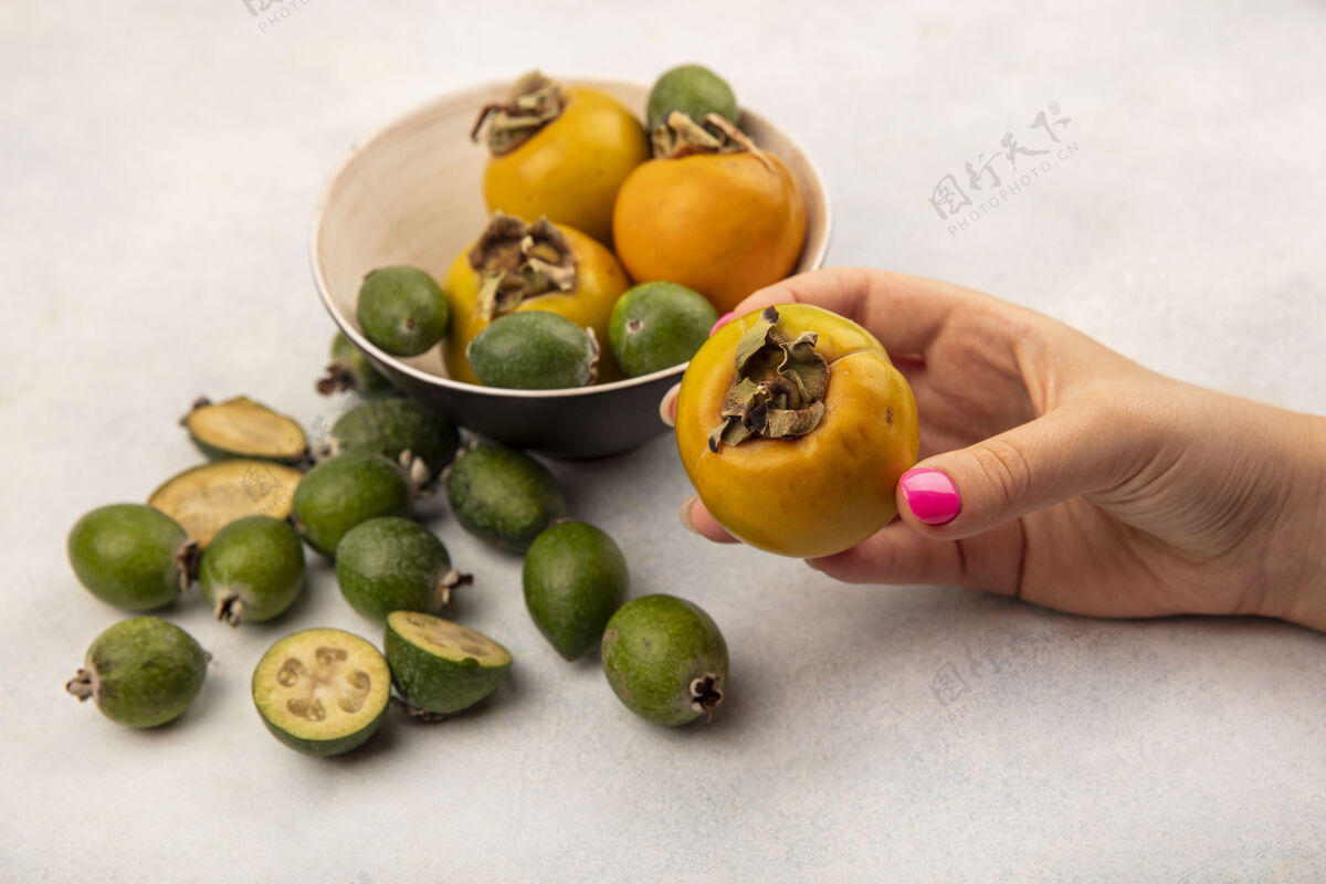 持有俯视图中的女性手拿着一个橙色成熟的柿子果实 在灰色的表面上隔离着飞珠和柿子新鲜营养美味