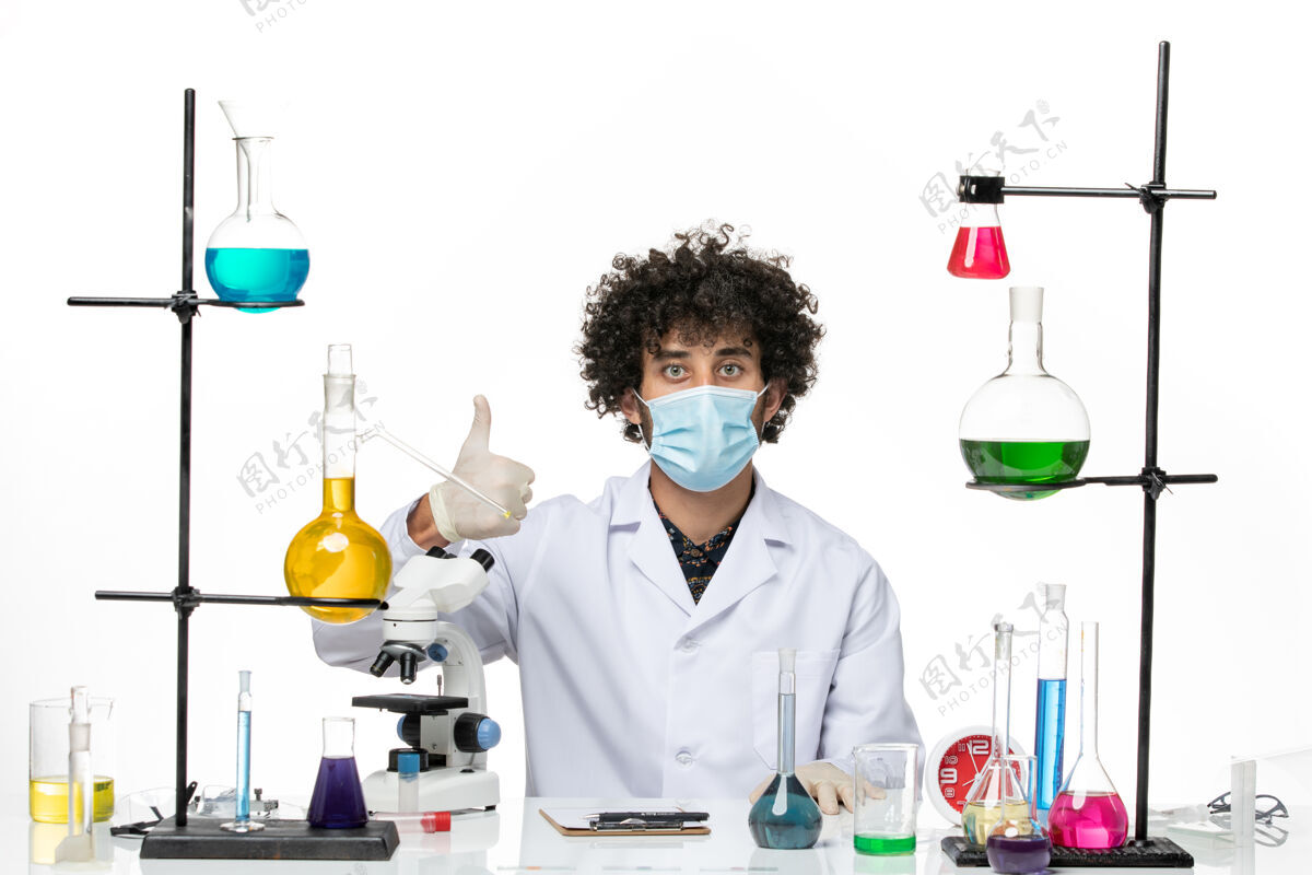 专业前视图男性化学家穿着白色的医疗服 戴着面罩 坐在一个白色的空间里 不同的溶液实验室外套面具科学