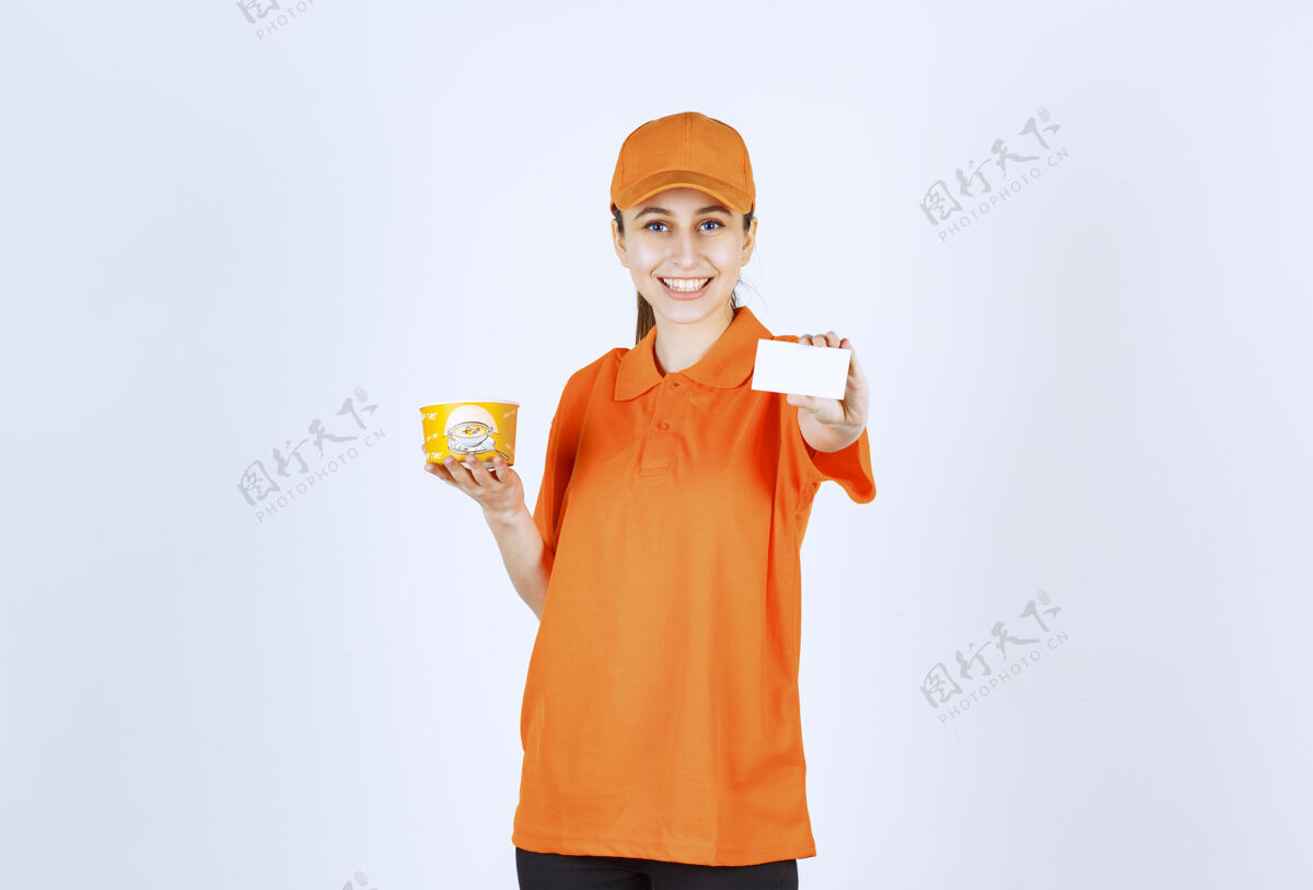 年轻人身着黄色制服的女快递员手持外卖面杯 出示名片姿势成人服务