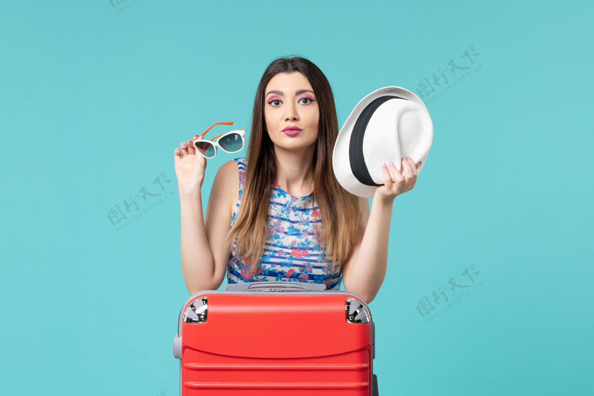 浅蓝色前视图美丽的女性手持太阳镜和帽子在淡蓝色的空间准备度假帽子海漂亮