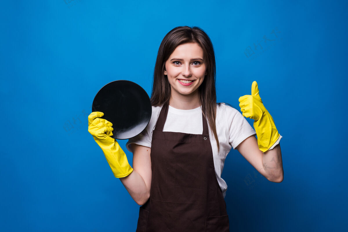 家用戴手套的年轻主妇展示海绵和干净的盘子隔离清洁盘子制服