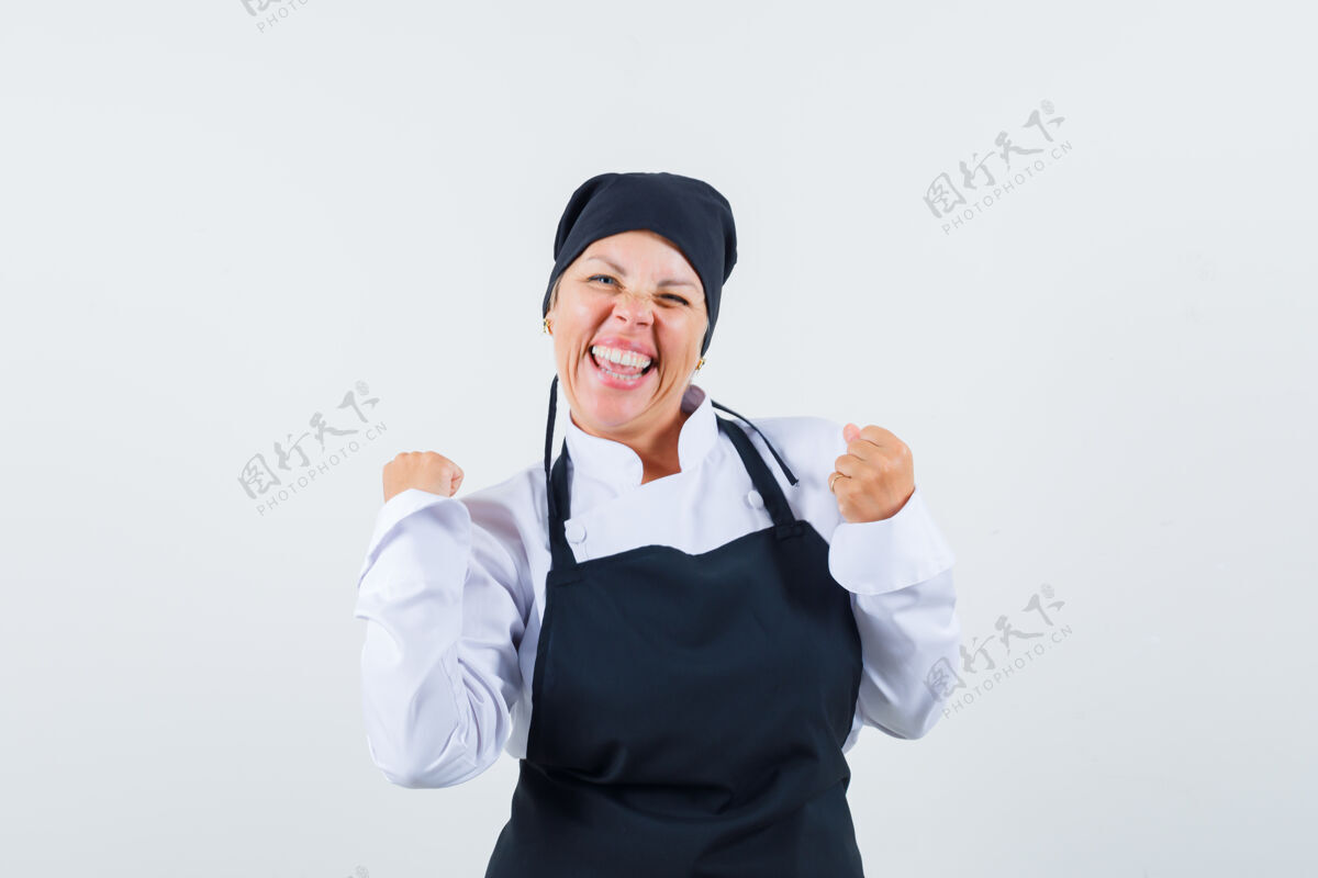 漂亮身着制服的女厨师 围裙 显示赢家的姿态 看起来很幸运 正面视图烹饪可爱皮肤护理