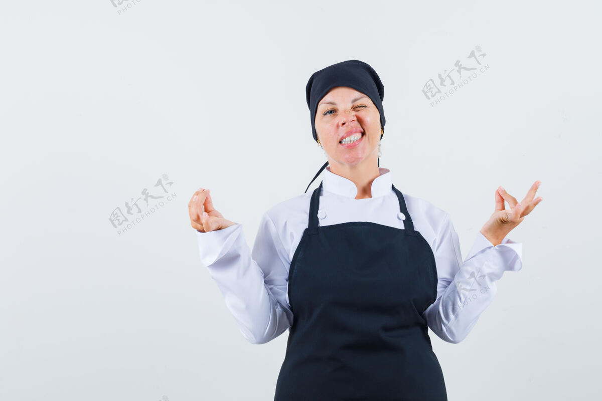 模特金发女人站在冥想的姿势 眨眼在黑色厨师制服 看起来很漂亮前视图站着自然女性